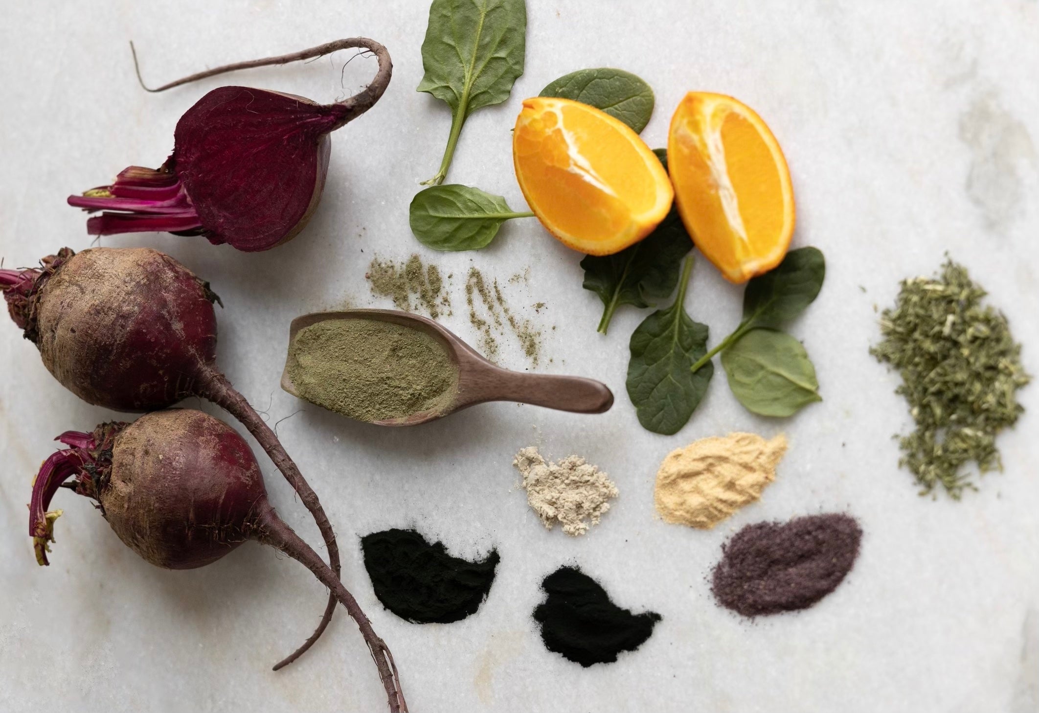 beets, oranges, spinach, and wellness powders scattered around